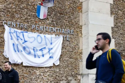 A banner reading 'death prison' hangs outside the La Santé penitentiary in Paris