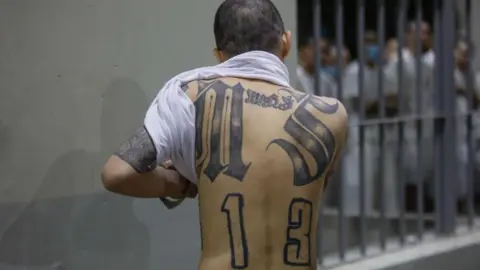 Getty Images An inmate shows his back tattoos at CECOT (Spanish acronym for counter-terrorism confinement center) in Tecoluca on February 6, 2024 in San Vicente, El Salvador. 