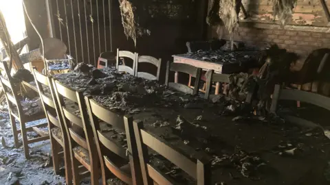 A table which is covered in ash, below the roof which has debris hanging off it. 