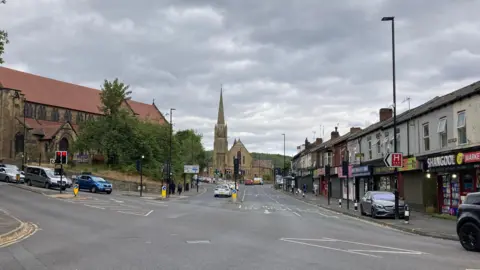 BBC / Jack Hadaway-Weller A crossroads with a number of vehicles on. In the background is a large sandstone coloured church.
