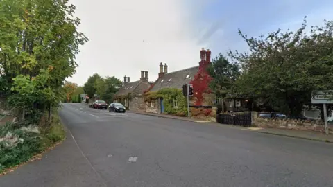 A road with cottages and cars stopped at traffic lights