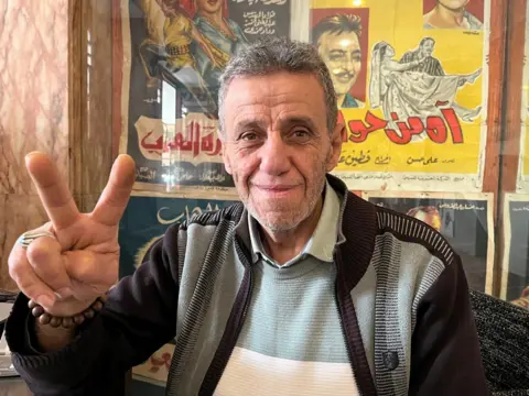 Mohamed makes a peace sign with his hands. 