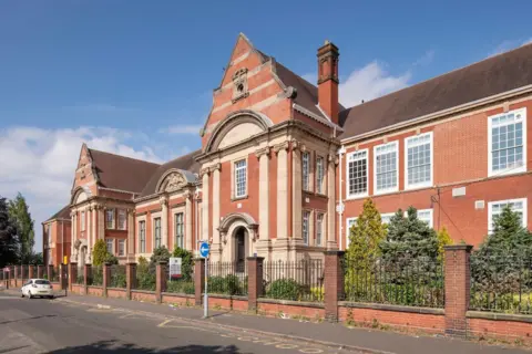 Historic England A red brick school with chimney and white windows with railings surrounding it.