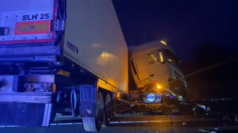 White HGV crashed at the side of a road at night.