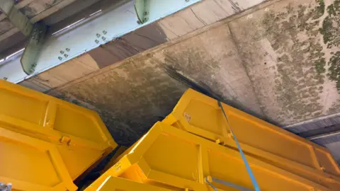 Network Rail A stack of yellow skips is wedged under a bridge.