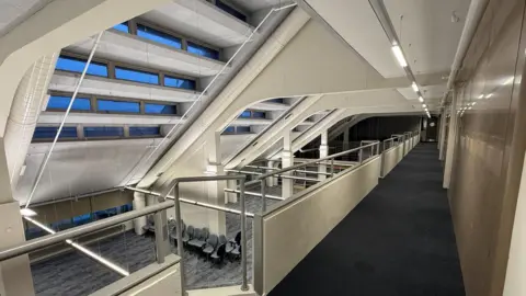 Cumberland Council View from the first floor of Carlisle Library looking onto the floor below. It is an open plan area, with new navy carpets and lots of office chairs lined up on the ground floor. 