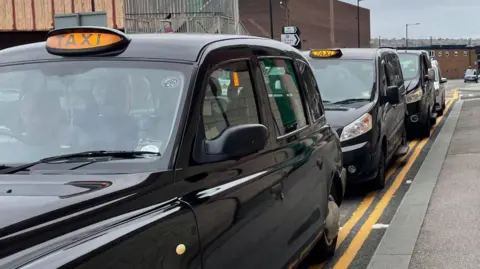 BBC/Simon Thake A row of black cabs waiting on double yellow lines