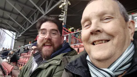 Malcom Townrow taking a selfie with his friend. They are both smiling at the camera and Malcolm is on the right.