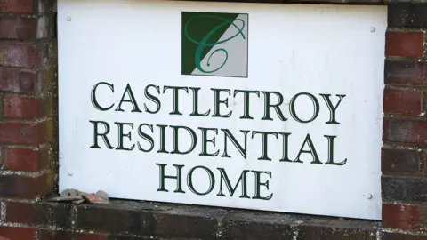 South Beds News Agency A sign for Castletroy Residential Home, in green writing, placed on a red brick wall. 