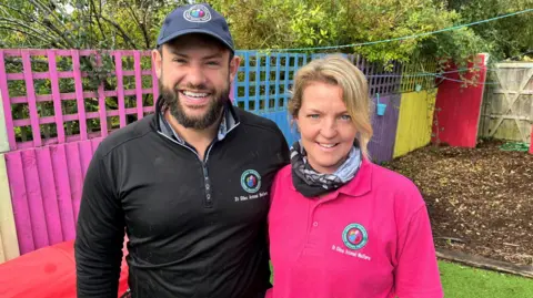 Jack, wearing a black top and cap, stood next too in Komala in a pink top, looking at the camera and smiling