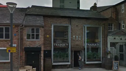 Google Maps Google Image street view of the bar. The building is a medium size brick building with black framed windows. Twp windows have 'Trader's' printed in white on the glass.