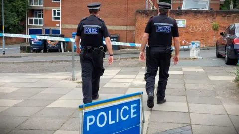 Two police officers dressed in black with their backs turned and a police sign in the foreground