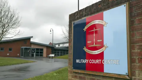 PA Media Entrance to Bulford Military Court Centre, with tricolour sign (navy blue, red and light blue to symbolise the navy, army and RAF). The sign reads 'Military Court Centre' and has a weighing scale in the middle, with scrolls above and below reading 'Military Court Service' and 'Independent and Impartial'