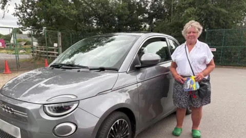 Susan Jenkins stood in front of her grey car. She is staring straight at the camera. 