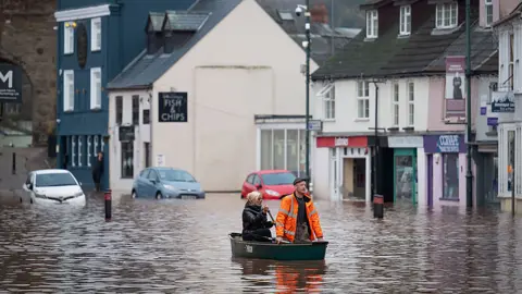 Two people use a boat to navigate along Monmouth high street