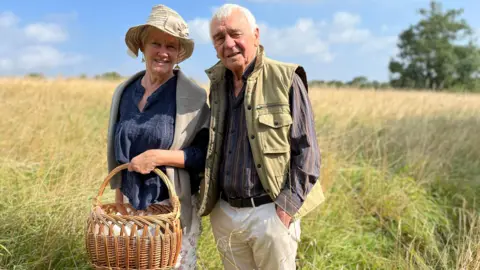 Shan Oakes carrying a basket standing next to Bill Rigby in a field