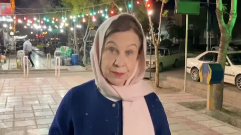 Lyse wears a navy jacket, pink headscarf as she looks into the camera