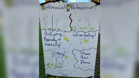 East Riding of Yorkshire Council A close up photo of Mia's sign which says 'anti-social behaviour' at the top with stick figures demonstrating anger with words such as 'bullying, physically or mentally', 'intimidating' and 'harass, alert, distress'.