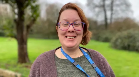 Charlotte Carr wearing glasses and smiling. She has short hair.