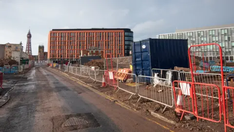 Red and silver fences cordon off building work with Blackpool Tower in the background