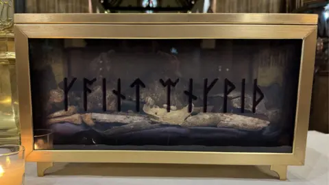 BBC/Jo Burn A gold framed glass box with human bones inside. The box is stood on a white surface. To the left is a small candle