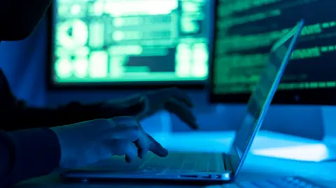 Getty Images A person typing into a laptop with two screens behind them