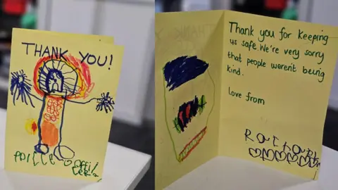 Northumbria Police Two cards made on yellow paper by a young child with a child's picture of a police officer and the words "thank you" on one and the words "thank you for keeping us safe - we're sorry that people weren't being kind" on the other.