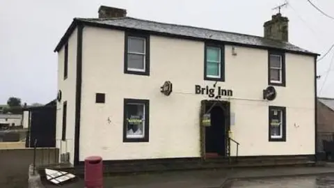 Brig Inn Pub & Hub The Brig Inn pub - a white two-storey building with black trim around the windows and chimney. 