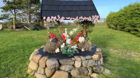 An example of what the memorial wishing well for Billy would look like. It is decorated with pants and flowers, with duck ornaments and a picture of Billy. His ashes are in a silver heart in the middle of the composition on top of the well.