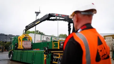 Travis Perkins Man in hard hat and hi-viz watches blocks being loaded onto a lorry