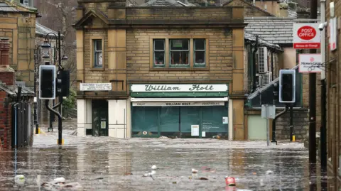 Christopher Furlong/Getty Images A shop in Hebden Bridge is submerged by flood water. Trash is floating in the water