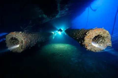 Niclas Andersson/UPY2026 The wreck of Japanese battleship, IJN Nagato, in the Bikini Atoll. The picture shows a diver with a torch light swimming between the twin stern guns