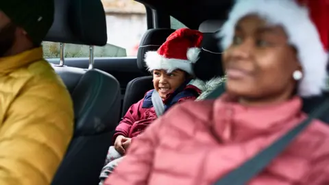 Getty Images Stock photo shows a mother and son wearing Santa hats sit in the front passenger seat and rear seat of a car with the father in the driving seat out of frame