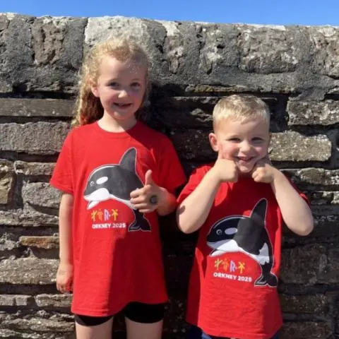 Two young children wearing t-shirts with an orca on them, the mascot for the island games