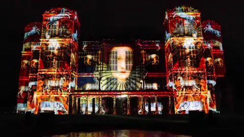 PA Media A portrait of Bess of Hardwick projected on to the outside of a stately home at night.
