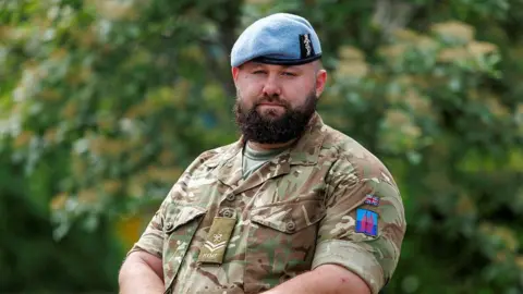 Sgt Anil Gurung Corporal Rhys Calland wears his Armed Forces uniform and looks directly at the camera with a serious expression