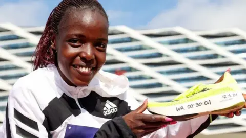 Getty Images Agnes Jebet Tirop holds a running shoe with the following handwritten on the side: WR 00:30:01