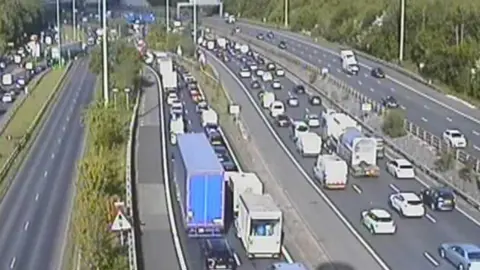 Highways England A motorway traffic camera image showing queueing cars, vans and lorries on the M60.