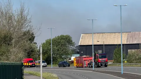the same building with three fire emergency vehicles parked on an empty two carriage motorway in front 