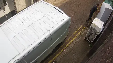 City of Wolverhampton Council A large white van is parked on a small city centre street, next to double-yellow lines. A man on the right can be seen holding a large fridge, which has been placed next to another one.