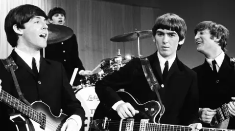 Getty Images The Beatles in black and white, with Paul McCartney, Ringo Starr, George Harrison, and John Lennon dressed in suits playing their instruments.