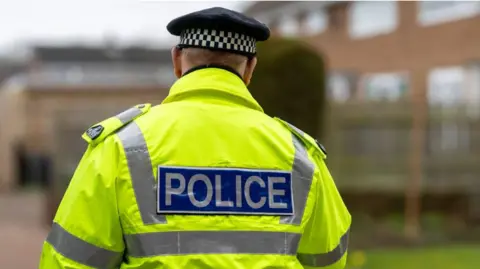 Getty Images The back of a police officer in a high-visibility neon yellow jacket with the word "Police" on the back.