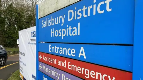 A close-up of a blue and red sign saying 'Salisbury District Hospital, Entrance A, Accident and Emergency'