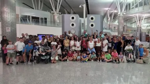 Family Handout A large group of people standing in an airport. There are people of all ages.