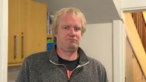 A man inside the kitchen of the foodbank. He looks serious. 