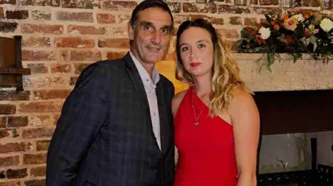 supplied Russell wearing a suit standing alongside Kayleigh in a red dress