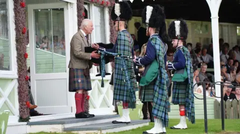 PA Media Charles in a brown kilt meets three bagpipers in green kilts and bearskin hats