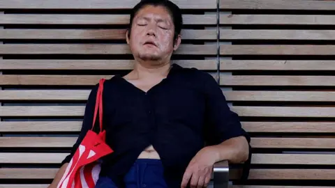 AFP via Getty Images A man rests in the shade on a bench in Midtown Manhattan during a heatwave in New York City on 3 July