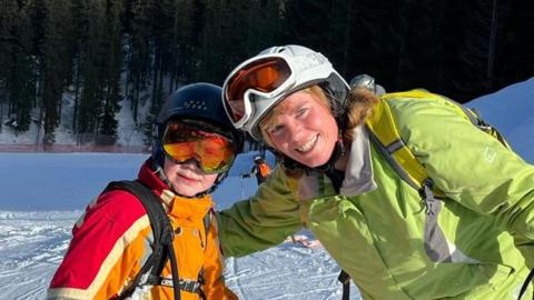 Mother, Julie with Son, Alex, in full skiing gear on a snowy mountain