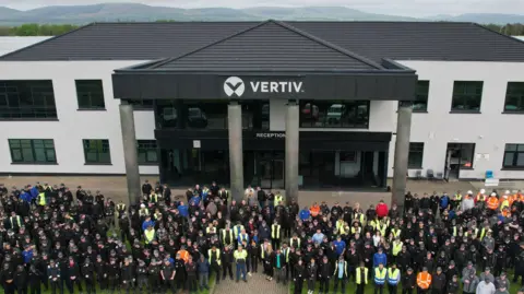 Vertiv A crowd of people are standing outside a large black and white building with a Vertiv sign at the top.